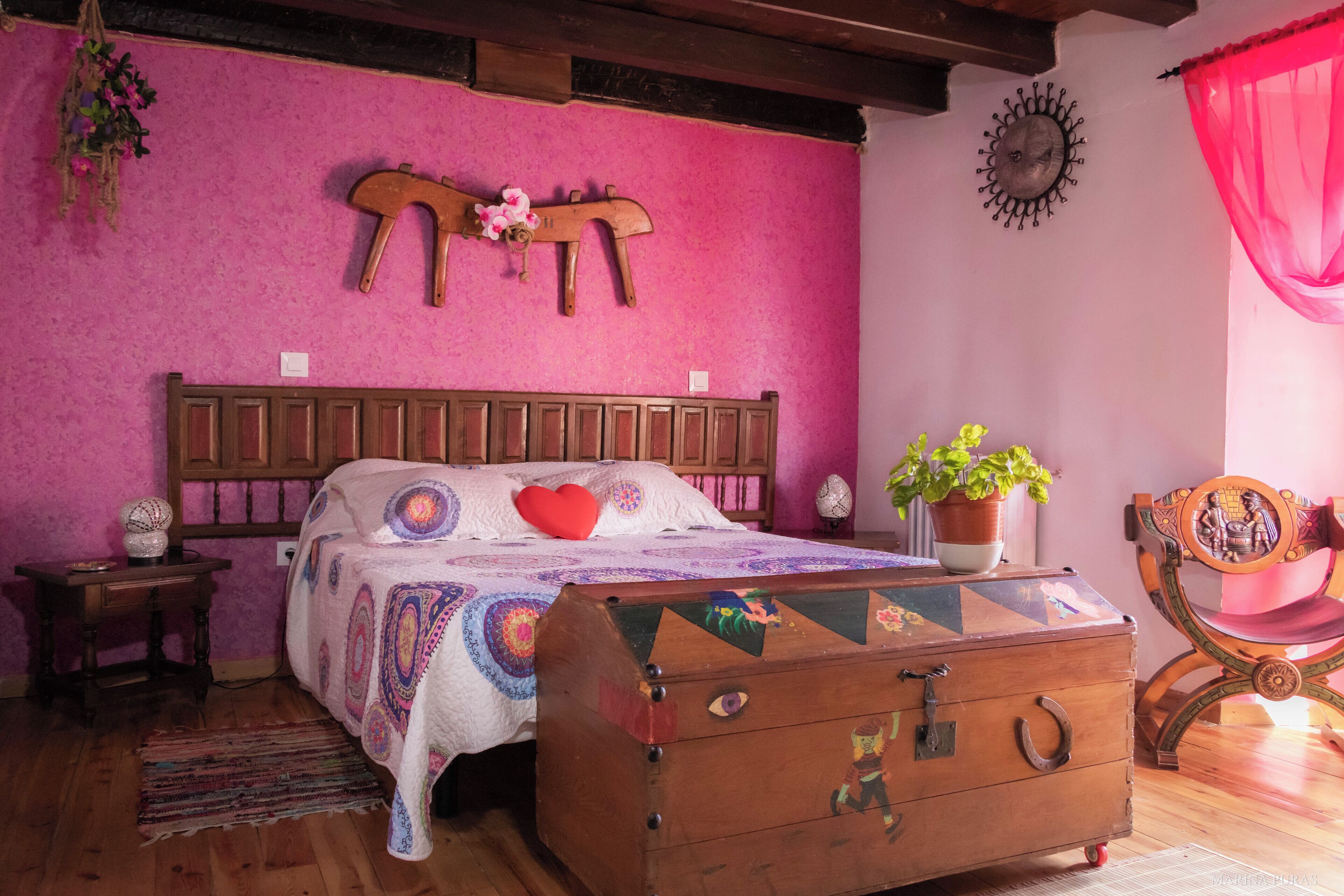 Un dormitorio con una cama de madera, un edredón colorido, un aparador de madera, una planta en maceta y una silla decorativa.