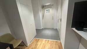 A hallway with a wooden floor, a white wardrobe, a television on a stand, and a door with a sign.