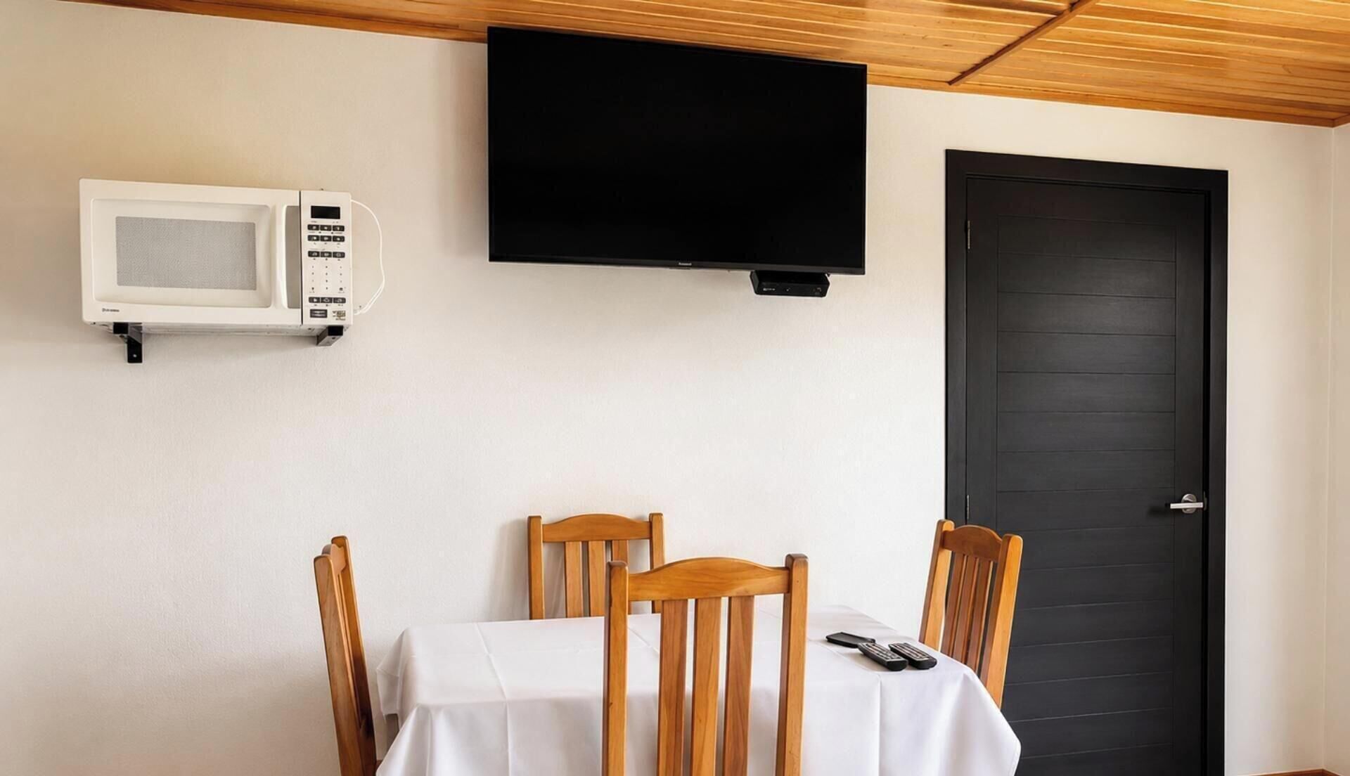 A room with a table, chairs, a television mounted on the wall, a door, and a microwave.