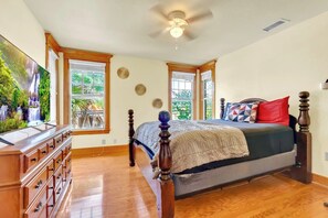 A bedroom with a large bed, wooden headboard, a ceiling fan, and a view of greenery through the windows. - Massive Porch Paradise - 5 mins to DT (Jacksonville)