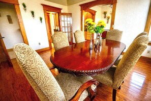 Comedor con una mesa redonda de madera rodeada por seis sillas estampadas, un florero con flores amarillas y una puerta de madera con un espejo.