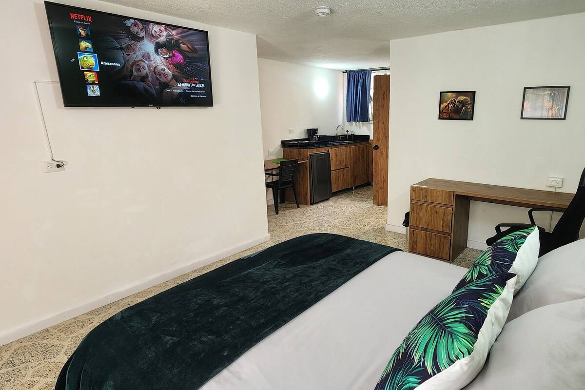 Une chambre d’hôtel équipée d’un lit, d’un bureau, d’une chaise, d’une télévision et d’une kitchenette.