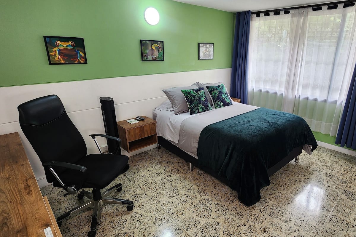 Une chambre à coucher avec un lit, une chaise, une table de chevet et une fenêtre avec des rideaux.