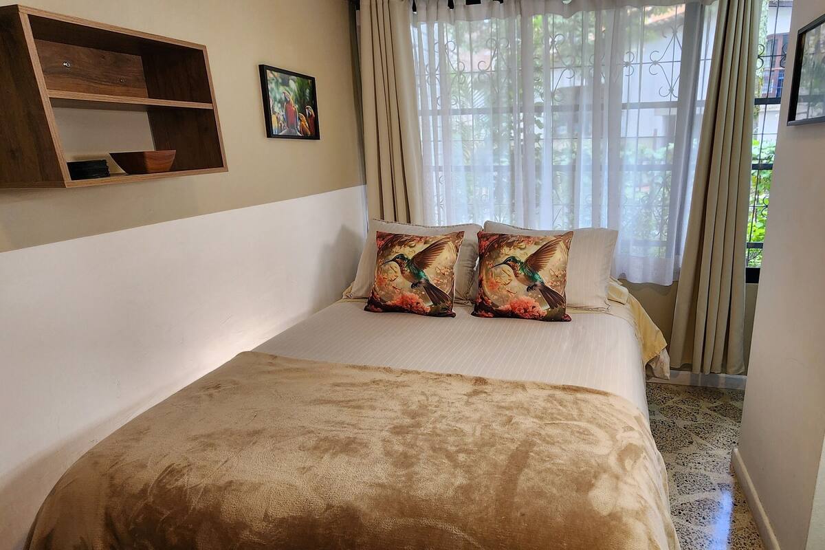 Une chambre à coucher avec un lit, des oreillers, une étagère en bois et une fenêtre avec des rideaux.