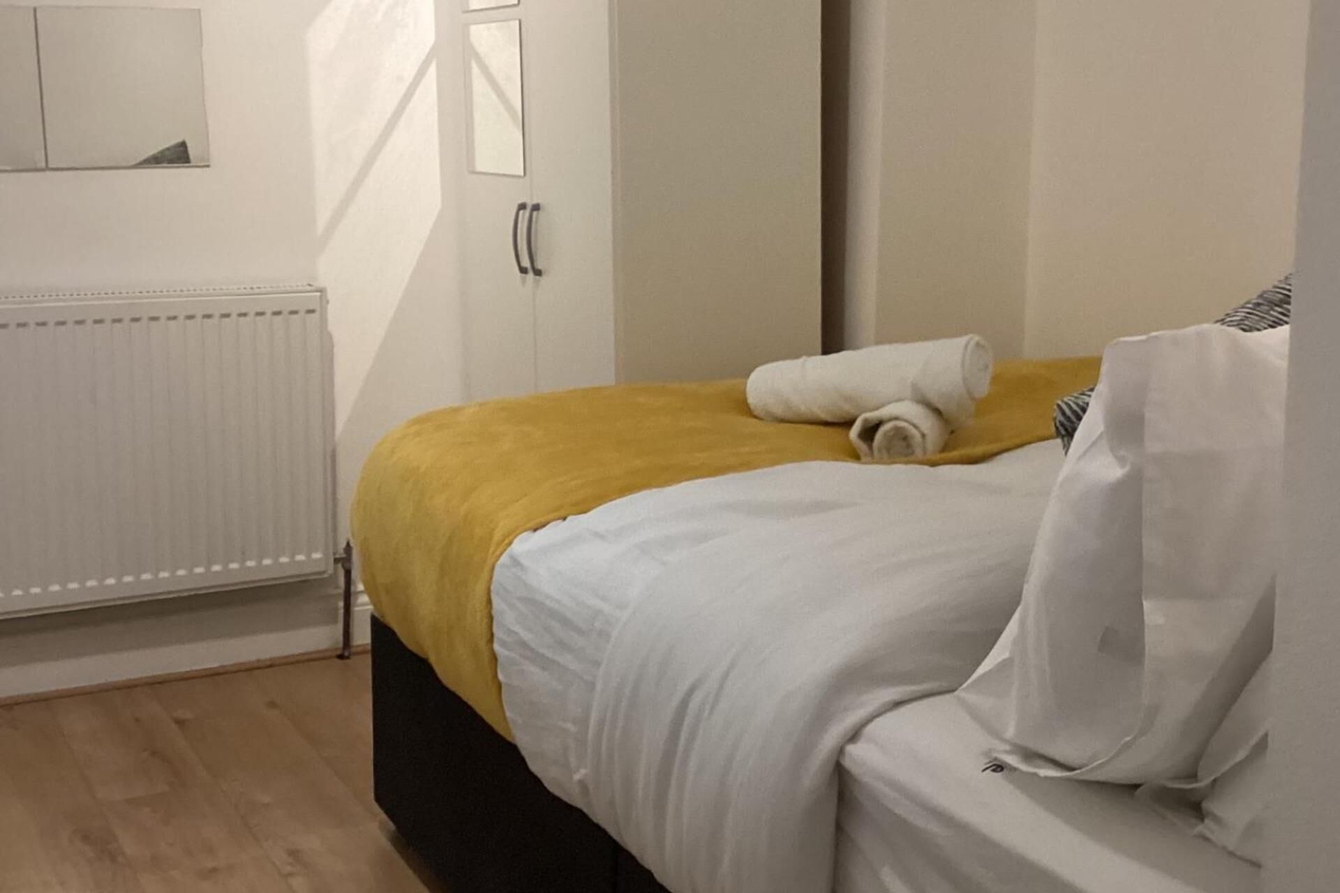 A hotel room with a bed, a yellow blanket, a white pillow, and a rolled towel.