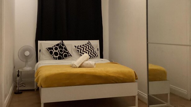 Una cama con estructura blanca, manta amarilla y dos almohadas estampadas.