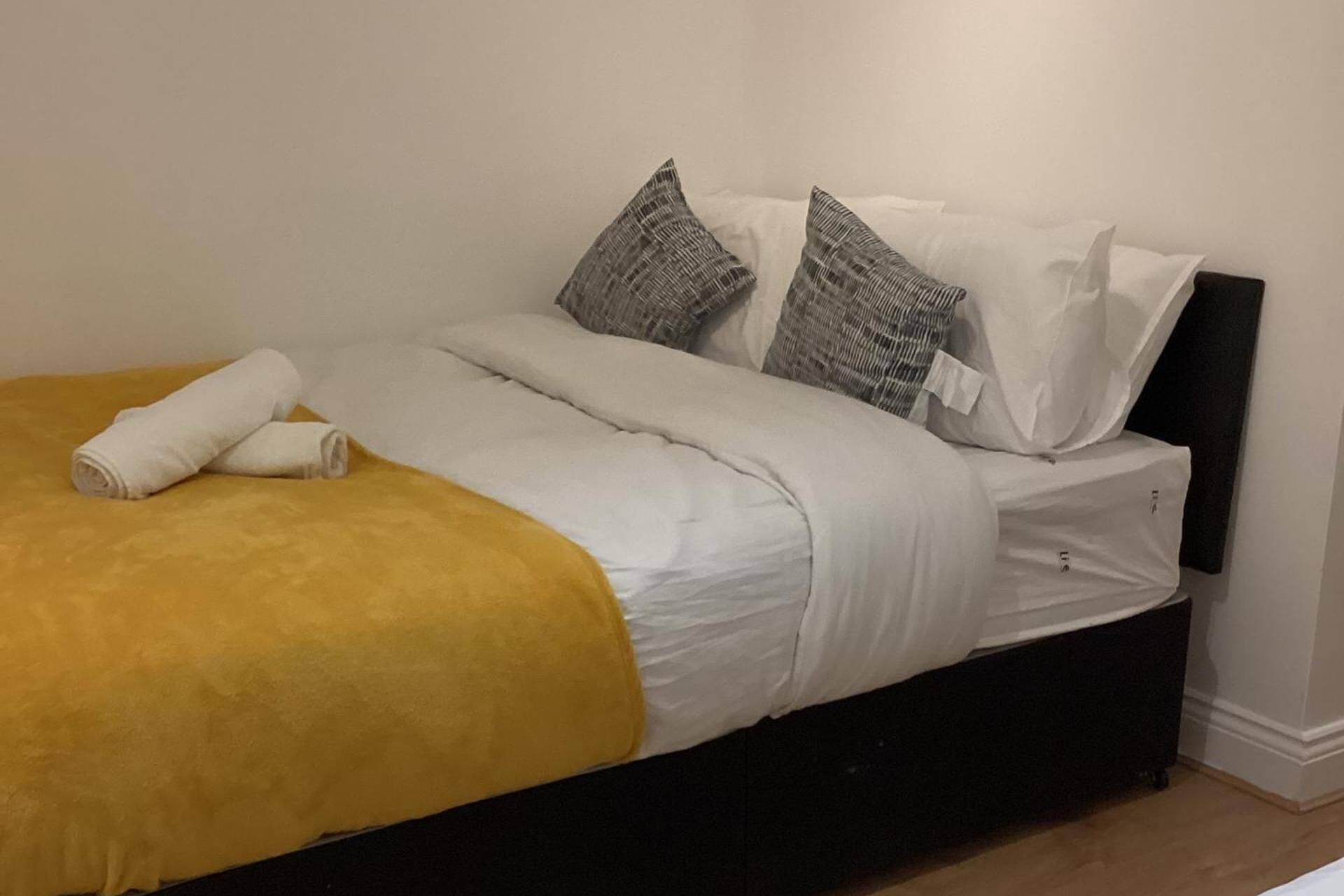 A bed with a yellow blanket, white bedding, and two patterned pillows.