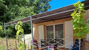 Ein Garten mit erhöhten Beeten, einer Pergola und einer Terrasse mit Stühlen und einem Tisch.