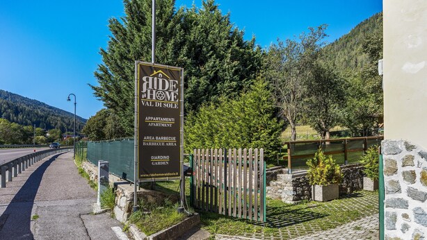Een bord met 'Ride Home Val di Sole', met genoemde faciliteiten zoals appartementen, barbecueplaats en tuin.