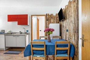 A modern kitchen with white cabinets, a red accent wall, a wooden dining table with blue chairs, and a wooden wall paneling.
