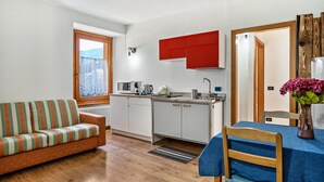 Ein kompakter Wohnbereich mit Küchenzeile, einer Couch, einem Esstisch und Blick durch ein Fenster.