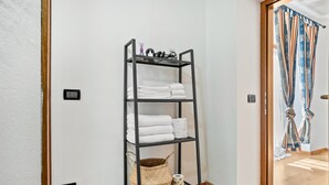 Ein schwarzes Metallregal mit weißen Handtüchern und einem gewebten Korb vor einer weißen Wand.