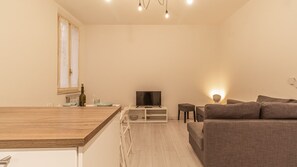 A modern living room with a sofa, a TV, and a dining area with a table and chairs. - La casa del Vicolo: 2 camere letto, Wi-Fi & A/C (Modena)
