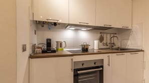 A modern kitchen with white cabinets, a built-in oven, a coffee maker, and a kettle on the countertop.