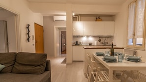A compact kitchen with a dining area, a sofa, and a wooden door. - La casa del Vicolo: 2 camere letto, Wi-Fi & A/C (Modena)