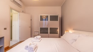A hotel room with a bed, a wardrobe, a small table, and a door leading to another room.