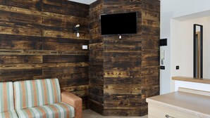 Una habitación con un panel de madera en la pared, un televisor de pantalla plana montado en la pared, un sofá con cojines a rayas y un aparador de madera.