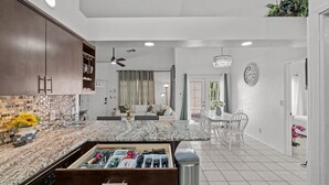 Una cocina moderna con encimera de granito, lavavajillas integrado y un comedor con mesa y sillas blancas.