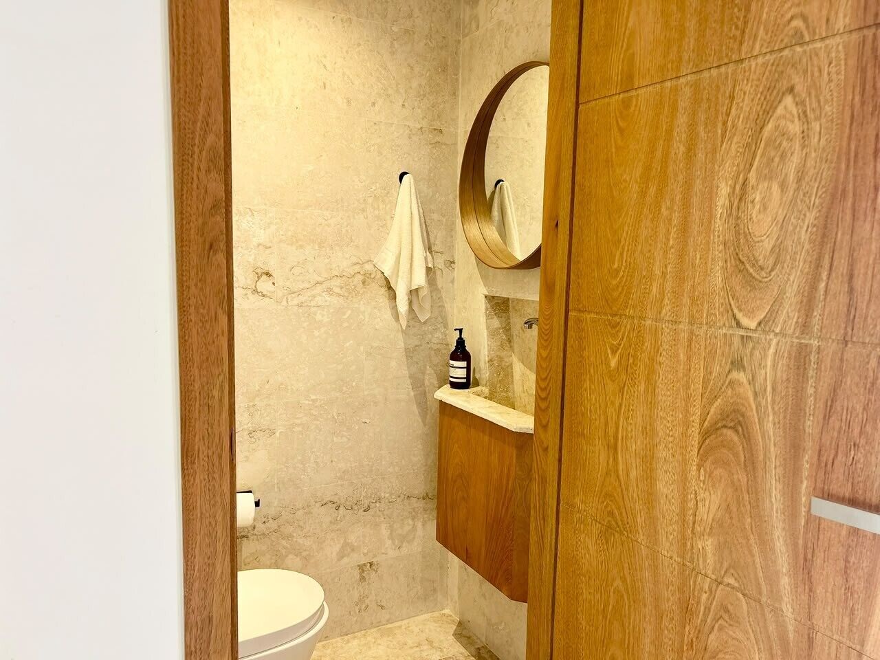 Une salle de bain avec des toilettes, un meuble-lavabo en bois avec un miroir et une serviette accrochée au mur.