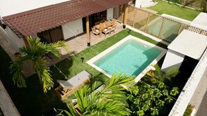 Une piscine dotée d’une terrasse en bois, entourée de palmiers et agrémentée d’un patio couvert.