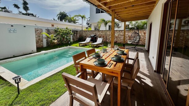 Un espace extérieur abrité, aménagé pour les repas, avec une piscine, des murs en pierre et une vue sur le jardin.