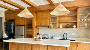Une cuisine moderne avec des meubles en bois, un grand îlot central, deux suspensions et un évier encastré.