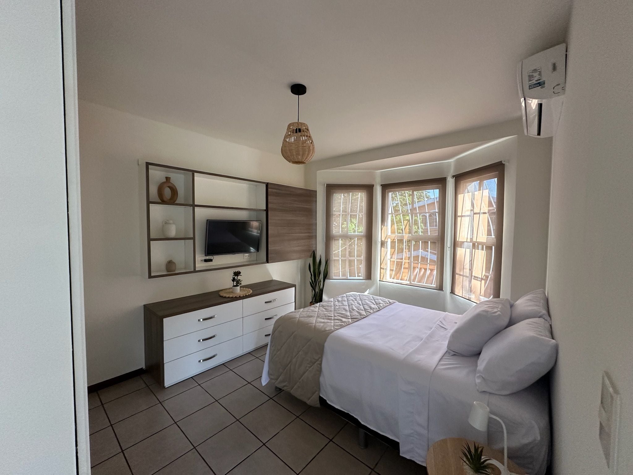 Una camera da letto con un letto, una TV, una cassettiera e una finestra.