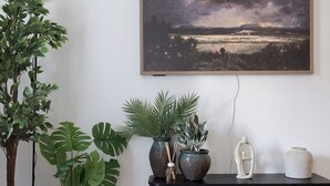 Una habitación con piso de madera, una consola de madera oscura con objetos decorativos y un gran cuadro de paisaje en la pared.