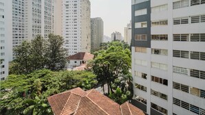 A high-rise building with multiple floors, surrounded by lush greenery and a smaller building with a red-tiled roof. - Eugenio Exclusive Stylish 1 BR in Sao Paulo (São Paulo)