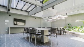 A modern outdoor dining area with a glass ceiling, metal chairs, and a central table. - Eugenio Exclusive Stylish 1 BR in Sao Paulo (São Paulo)