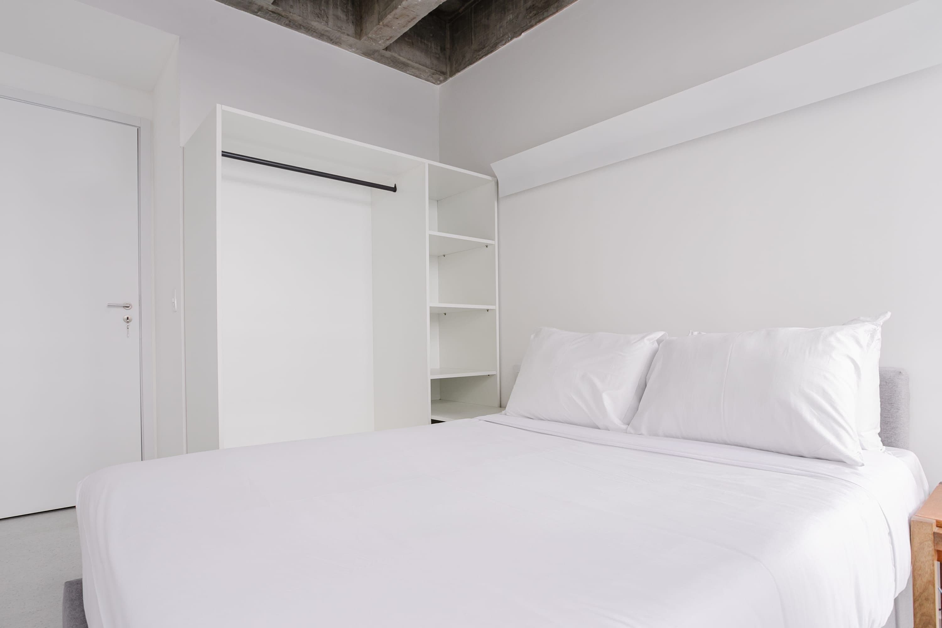 A bedroom with a bed, white walls, and a closet with open shelves.