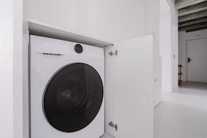 Un lavadero moderno con lavadora de carga frontal, una puerta con manija de metal y un techo visible con vigas a la vista.