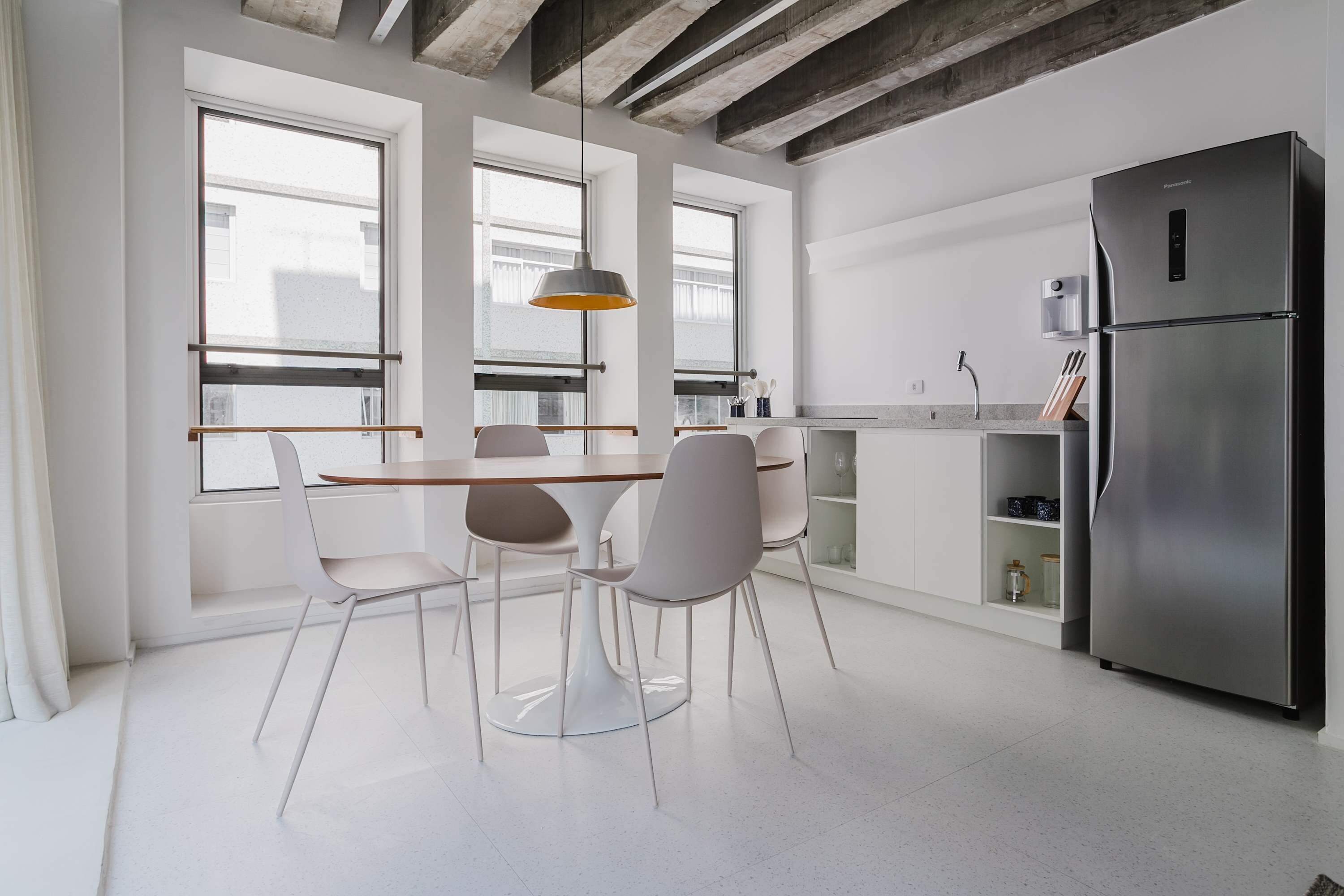 A modern kitchen with a dining table, chairs, a refrigerator, and large windows.