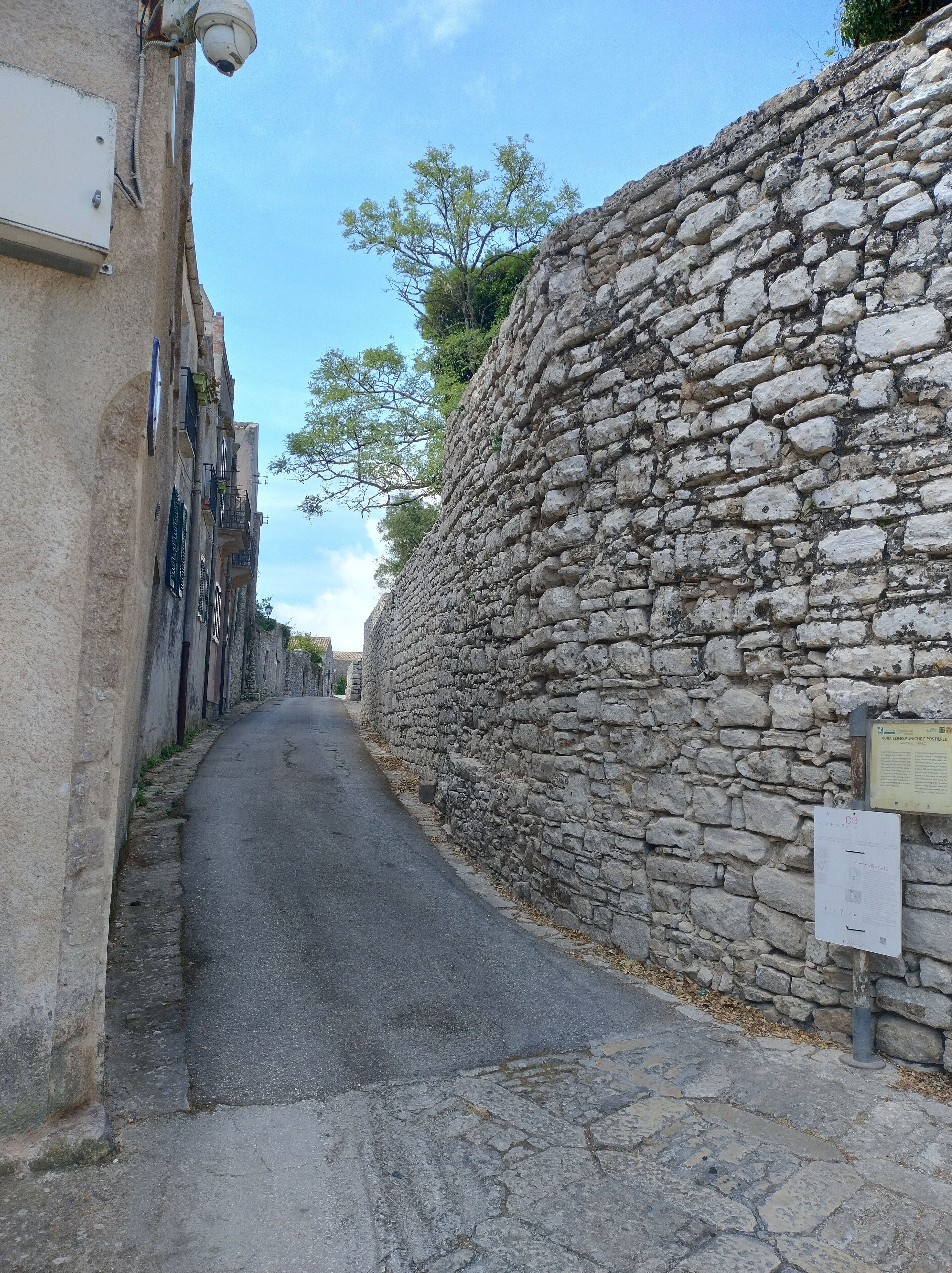 Eine enge Straße, begrenzt von Steinmauern und Gebäuden mit Balkonen.