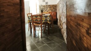 Vue intérieure d’un coin repas, avec une arche en bois rustique, une table entourée de chaises et un mur en pierre.