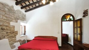 Une chambre avec un lit en bois, un mur en pierre et un plafond en pente avec des poutres apparentes.