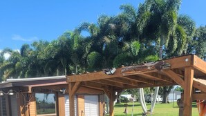 Une terrasse en bois avec une pergola, un espace salon extérieur et un petit coin cuisine.