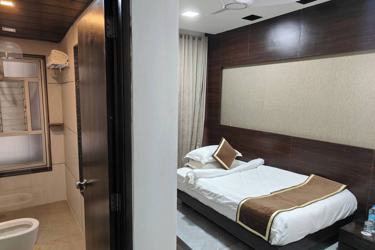 A hotel room with a bed, a bedside table with a water bottle, a bathroom with a toilet and a towel rack.