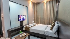 Ein Hotelzimmer mit Bett, Fernseher, einem kleinen Tisch mit Vase und Teller sowie einem Vorhang.