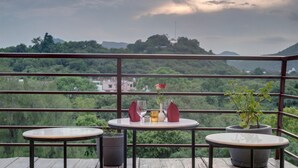 Ein Balkon mit zwei Tischen, jeder Tisch mit einem Topf und einer Pflanze, einem Glas Wasser und einer roten Serviette.