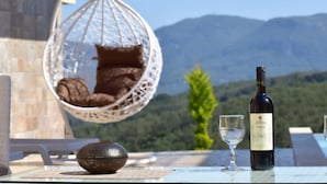 A table with a wine bottle and a glass, a hanging chair with cushions, and a view of mountains. - Pantokrator Private Pool Gem - Lux Villa in Corfu (Corfu)