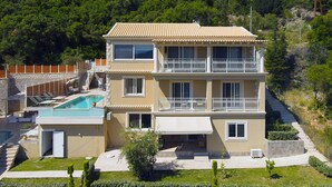 Un edificio de dos plantas con piscina, balcones y montañas al fondo.