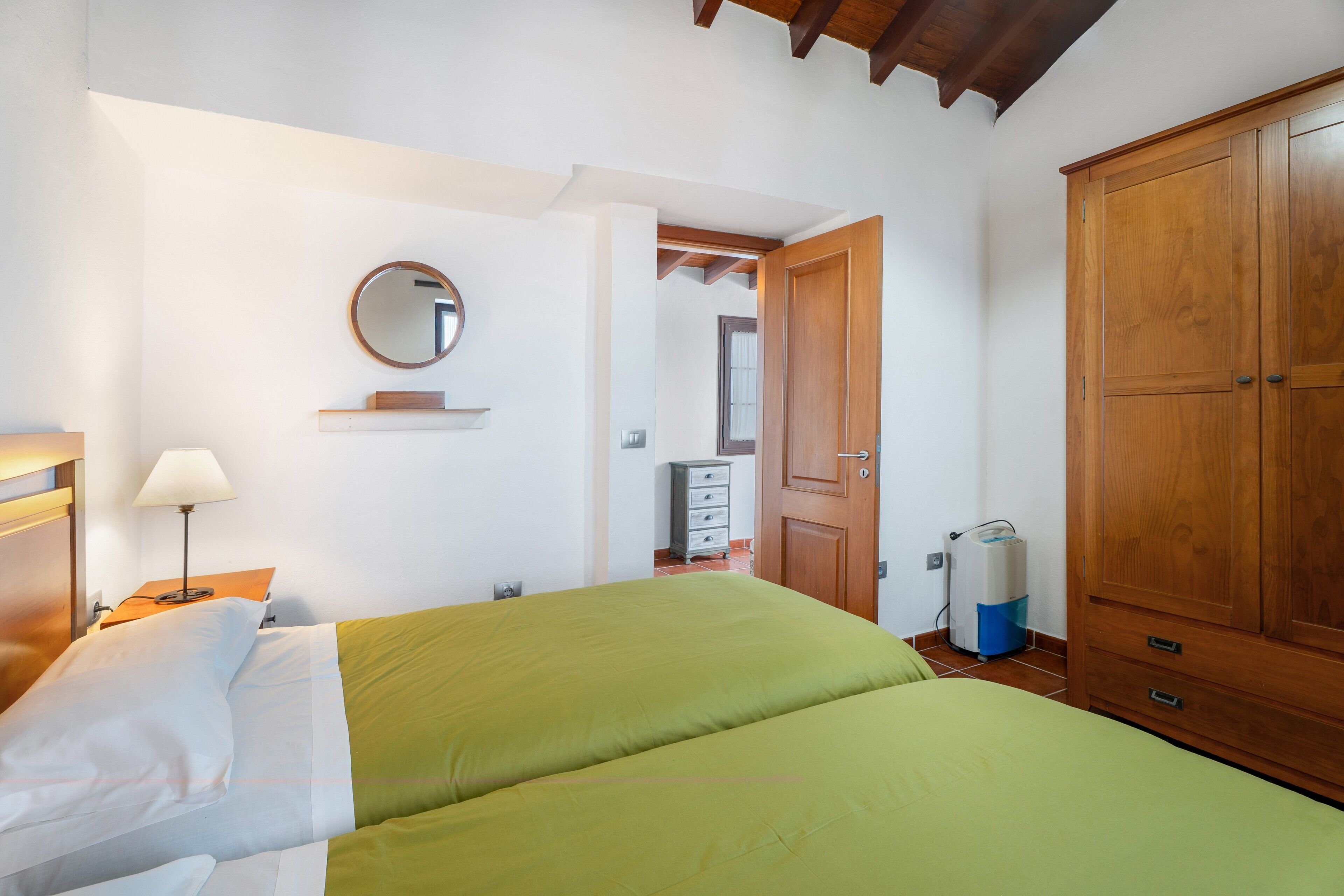 A bedroom with a bed, a bedside table with a lamp, a wardrobe, a mirror, and a small dresser.