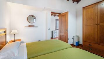 A bedroom with a bed, a bedside table with a lamp, a wardrobe, a mirror, and a small dresser.
