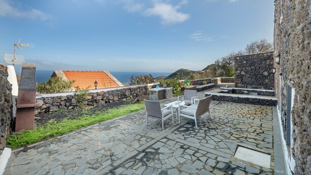 Un patio in pietra con mobili da esterno, un muro in pietra e vista sul mare.