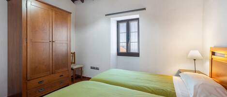 Un dormitorio con dos camas, un armario de madera, una ventana y una mesita de noche con lámpara.