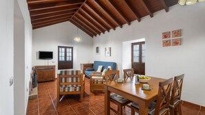 Un'ampia zona giorno con un tavolo da pranzo in legno, sedie, un divano e un televisore fissato alla parete.