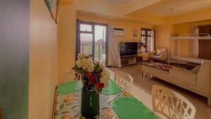 Un salon avec un téléviseur, un canapé et des lits superposés. On y trouve une table à manger avec des chaises et un vase de fleurs.