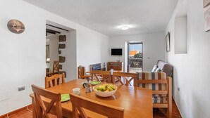 A dining area with a wooden table, chairs, and a bowl of fruit. There is a television mounted on the wall and a window providing a view outside. - Apartment El Peral in 'Casa Rural Los Perales' with Sea Views, Shared Terrace and Wi-Fi (Mocanal)