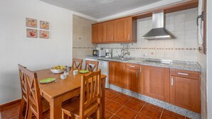 A kitchen with wooden cabinets, a granite countertop, and a dining table with chairs. - Apartment El Peral in 'Casa Rural Los Perales' with Sea Views, Shared Terrace and Wi-Fi (Mocanal)
